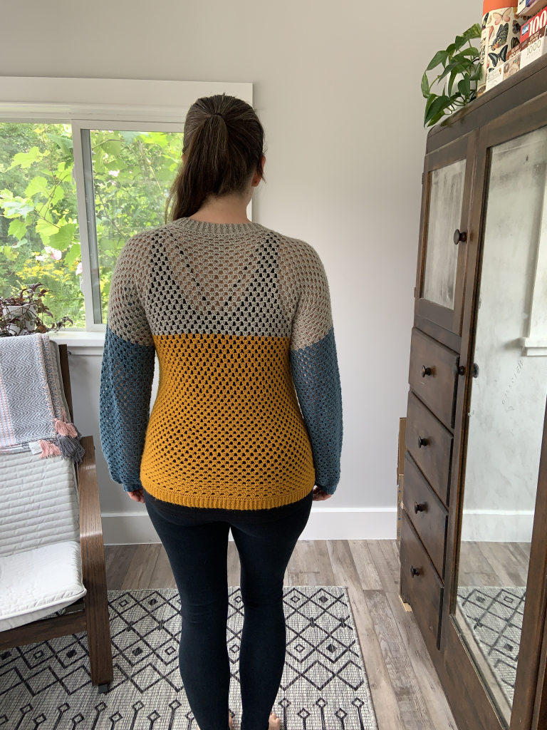 Back view of maker in finished crochet pullover in teal, ochre and grey