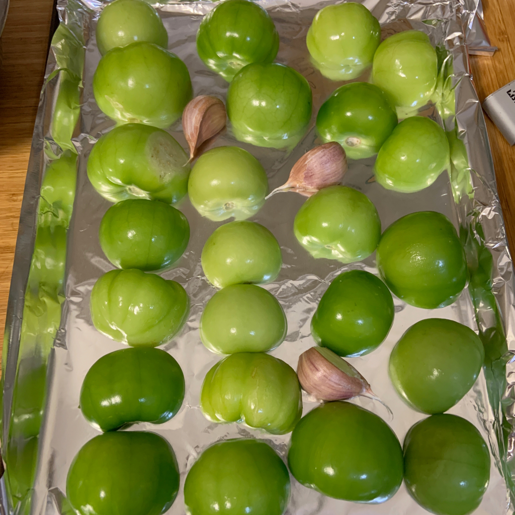 Tomatillos cut side down on a baking sheet with garlic cloves